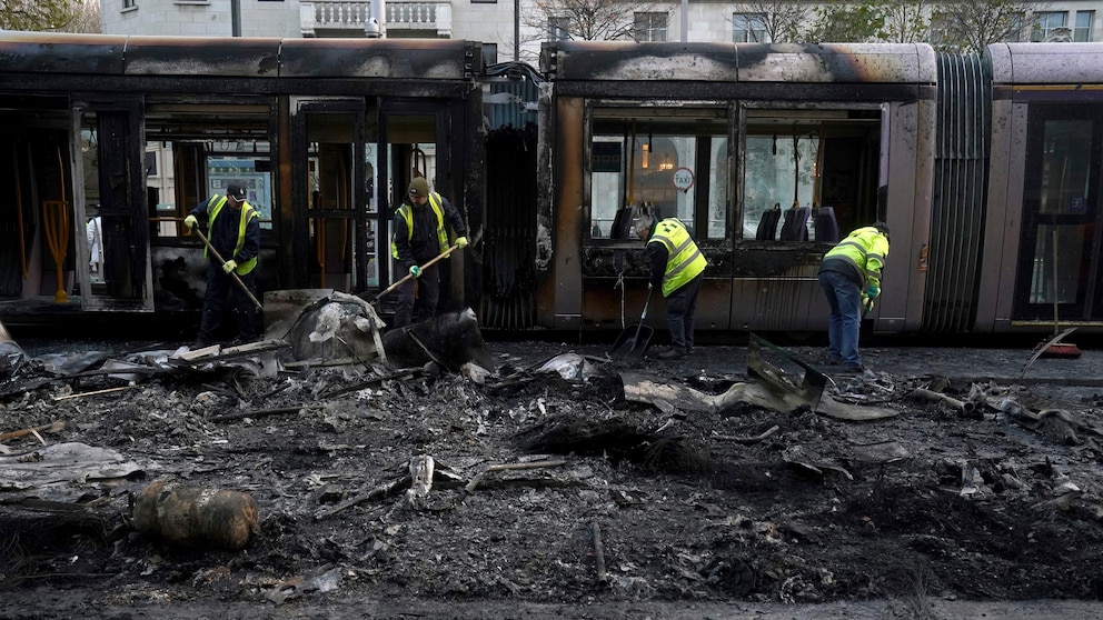 Debris is cleared from a burned out Luas and bus on O'Connell Street, in the aftermath of violence in the city center on Thursday evening, in Dublin, Friday, Nov. 24, 2023. The unrest came after an attack on Parnell Square East where five people were injured, including three young children. (Brian Lawless/PA via AP)